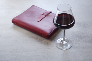 赤ワインを飲みながら、ワインレッドの革のシステム手帳に日記をつけているイメージ

