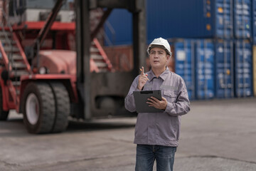 A logistics worker in a gray uniform inspects stacked shipping containers while holding a tablet. The image captures the precision and technology used in global supply chain management.