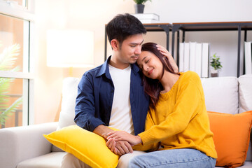 Portrait young asian couple hold hands sitting on sofa looking affectionate and embrace in living...