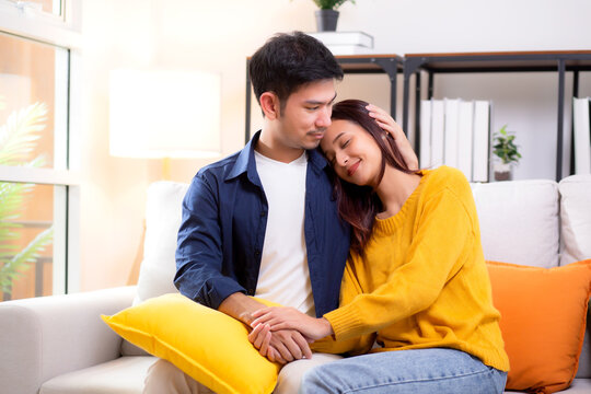 Portrait young asian couple hold hands sitting on sofa looking affectionate and embrace in living room at home, husband and wife with gentle and relation with cozy and love, couple and lifestyle. - Powered by Adobe