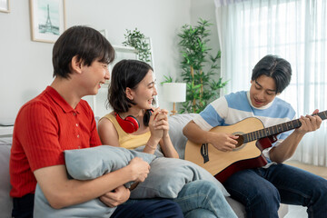Diverse Asian friends playing guitar and dancing in living room at home. 