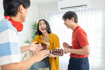 Diverse Asian friends playing guitar and dancing in living room at home.