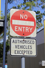 No Entry - Authorised Vehicles Excepted road sign against a backdrop of trees and a building