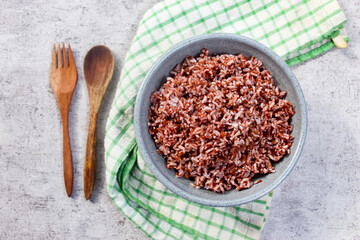 a bowl of cooked brown rice on the table with a spoon and fork