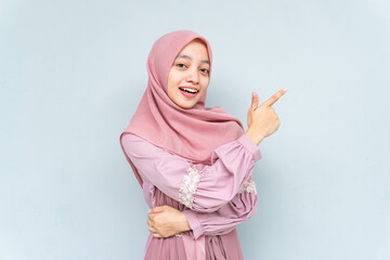 Asian Muslim young woman wearing headscarf veil hijab smiling cheerfully while looking and pointing...