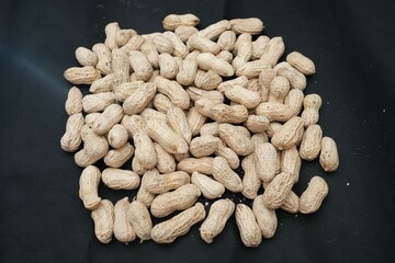 Pile of whole roasted peanuts in shells, densely arranged on a dark background, ideal for use in...