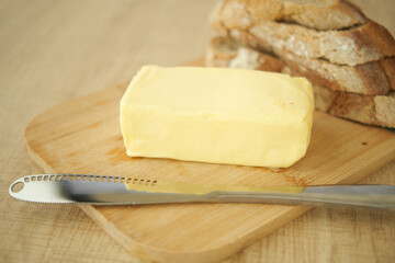 Butter on wooden board next to sliced bread with knife