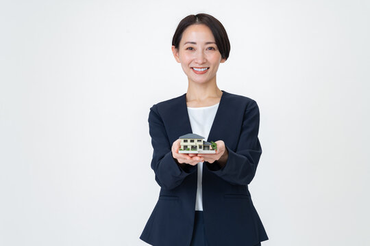 家の模型を持ち笑顔でカメラ目線のビジネスウーマン