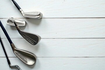 Golf clubs arranged on whitewashed wood tabletop, ample copy space , wedge, table
