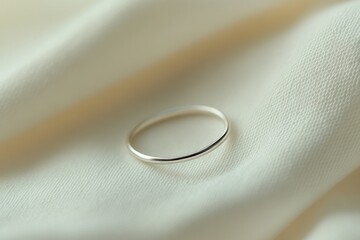 close-up of thin silver ring placed on white linen fabric soft folds adding texture and depth