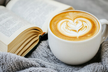 A steaming latte in an artistic ceramic cup, with vibrant latte art resembling an open book, placed beside a classic novel with copy space. 