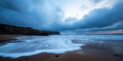 Dramatic sea waves crash onto a stormy beach, with imposing cliffs in the background setting a striking contrast against the turbulent sky.