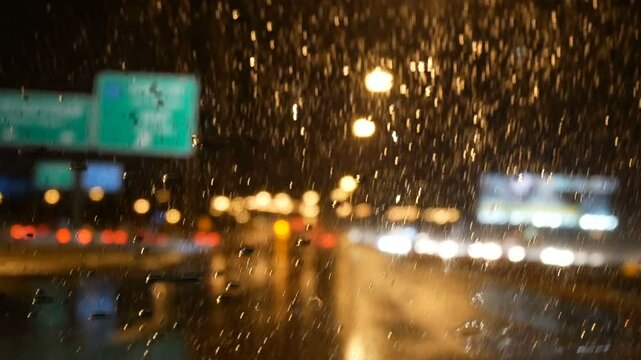4K. rain running down on front car window at night with bokeh of street light and traffic light on the road