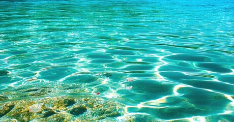 Crystal clear blue lagoon soft jade green undertones sharp sunlight refracting gentle ripples plastic wrappers drifting unnoticed tide