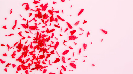 Scattered red fragments on a light background, creating a textured and abstract pattern with a sense of fragility and vibrant color.