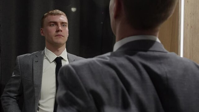 Young businessman in a suit adjusting his tie in front of a mirror, preparing for a business meeting or presentation, concept of self confidence and preparation in the business world