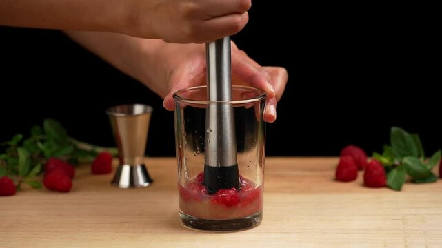 Preparing a raspberry mojito, mashing raspberries with a muddler to prepare a mojito