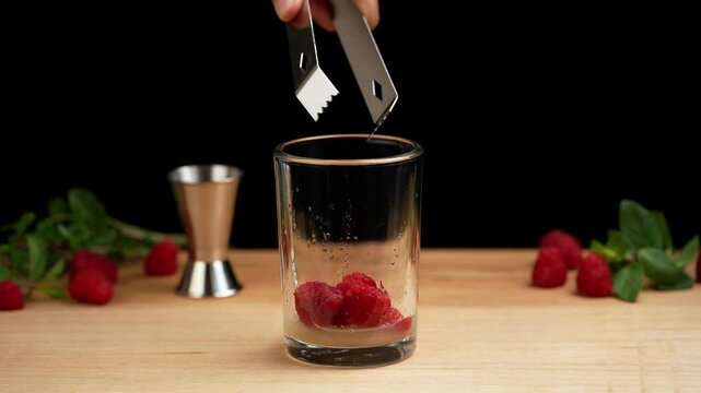 Preparing a raspberry mojito, raspberries falling into a glass to prepare a mojito