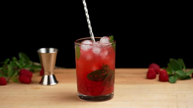 Preparing a raspberry mojito, stirring a mojito cocktail with a mixing spoon