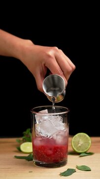Vertical video Raspberry mojito cocktail, pouring rum with a jigger to prepare a mojito