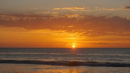 Obraz premium Beautiful Orange and Yellow Sunset Over the Ocean with Gentle Waves and Dramatic Clouds at Dusk