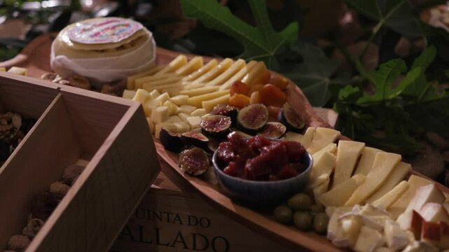 Wooden board with assorted cheeses, figs, olives, dried fruits, and jam in a rustic setting