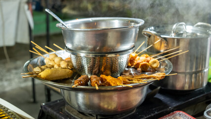 Steamed skewered snacks at a street food stall, served hot in stainless steel bowls. A mix of fish balls, sausages, and tofu, creating a warm, savory aroma in the bustling night market.