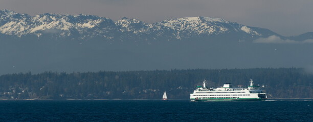 Ferry and sail boat passing Bainbridge island  framed by snowcaps on Olympic Mountains
