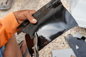 Obraz premium Close-up of a worker's hand using tin snips to cut a glossy black sheet metal piece. Scratches and markings on the metal indicate precision work. The textured background contrasts with the shiny