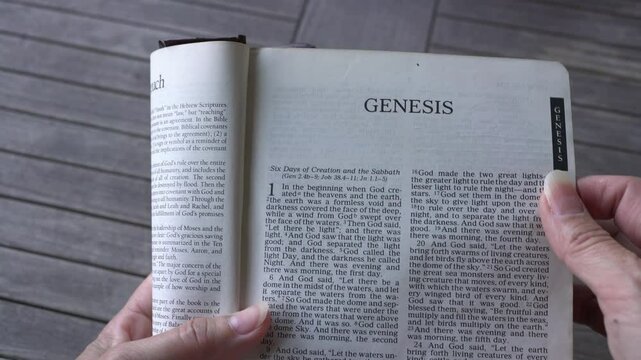 Picking the Holy Bible up from table with the Book of Genesis Chapter 1 open up, first line starting with In the beginning. Passage on the creation.