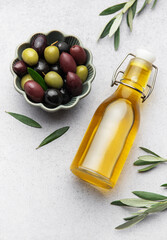 Olive oil bottle and bowl of green and black olives with olive branches on marble background