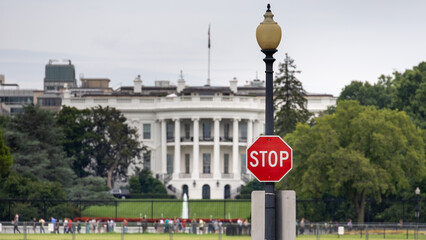 A stop sign in front of the White House in Washington DC, creating a symbolic contrast between authority and restrictions like military aid to Ukraine during the Russian war.