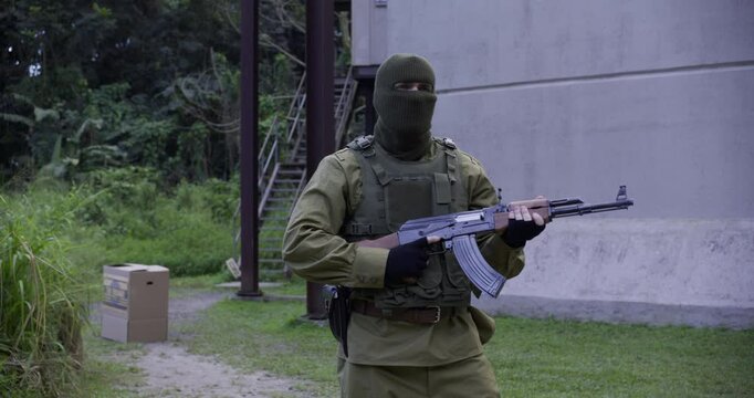 Suspicious guard with ak-47 looking around as person in box sneaks up on him