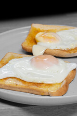 Fried egg on toast on a grey stoneware plate with a wooden board background. Traditional breakfast food concept.