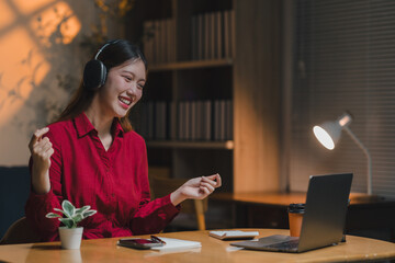 Young asian businesswoman wearing headphones enjoying music during a night work session