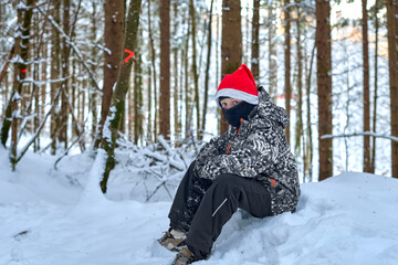 Fototapeta premium Winter Forest Portrait of Child in Santa Hat and Snow Gear Standing on Snowy Path Among Snow Dusted Trees in Magical Evening Light