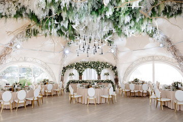 Elegant wedding reception hall featuring round tables, white and gold chairs, and floral arrangements
