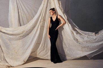 fashion model showcases a black dress, striking a poised pose beside a white, intricately draped...