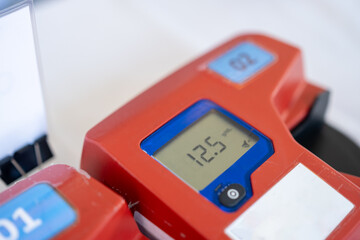 A close-up of a red medical device with a digital screen displaying a reading of 12.5. The device is used for health diagnostics and monitoring in a clinical setting.