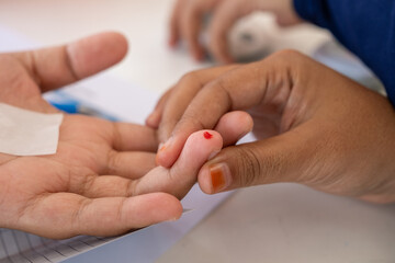 Close-up of a patient's fingertip with a fresh blood drop after a fingerstick test. A healthcare professional holds the finger gently, preparing for a medical examination or blood glucose test.