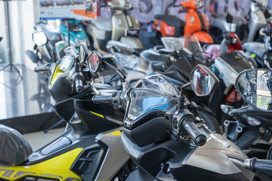 Close-up view of modern Yamaha scooters displayed in a showroom, featuring sleek designs, advanced digital dashboards, and ergonomic handlebars. Various models and colors are showcased