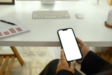 Close up view of business woman in black suit holding a smartphone with white screen sitting at desk