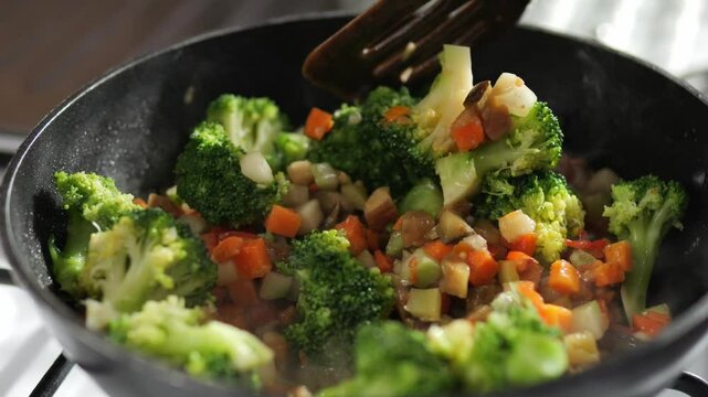 Defrosted vegetable stew is cooked in a frying pan. A vegetarian dish made with chopped vegetables and broccoli.