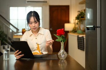 Young asian woman enjoys a plate of spaghetti and reading or browsing on digital tablet