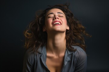 Fototapeta premium With her head tilted back and a wide smile, a woman exudes pure joy in a dimly lit indoor space. The atmosphere feels intimate as her curly hair dances around her, reflecting a sense of freedom