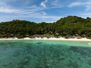 A hill with dense greenery overlooks a clear sea and sandy beach with coral reef. Koh Tao, Thailand.
