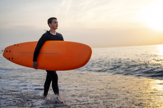 Happy young man is carrying surfboard walking on the beach. Sport, people, summer vacation concept