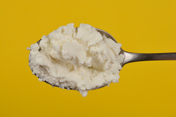 A close-up shot of a spoonful of creamy white cottage cheese against a yellow background, showcasing its lumpy texture
