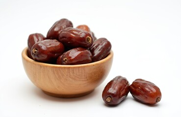 Obraz premium Dry dates palm in wooden bowl isolated on white background. Healthy sweet organic fruit snack for breakfast. Traditional arabic islamic food culture. Delicious ramadan dessert treat.