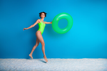 Joyful woman in green swimsuit holding float against clear blue background, showcasing summer fun, bright energy, and beach vacation vibes